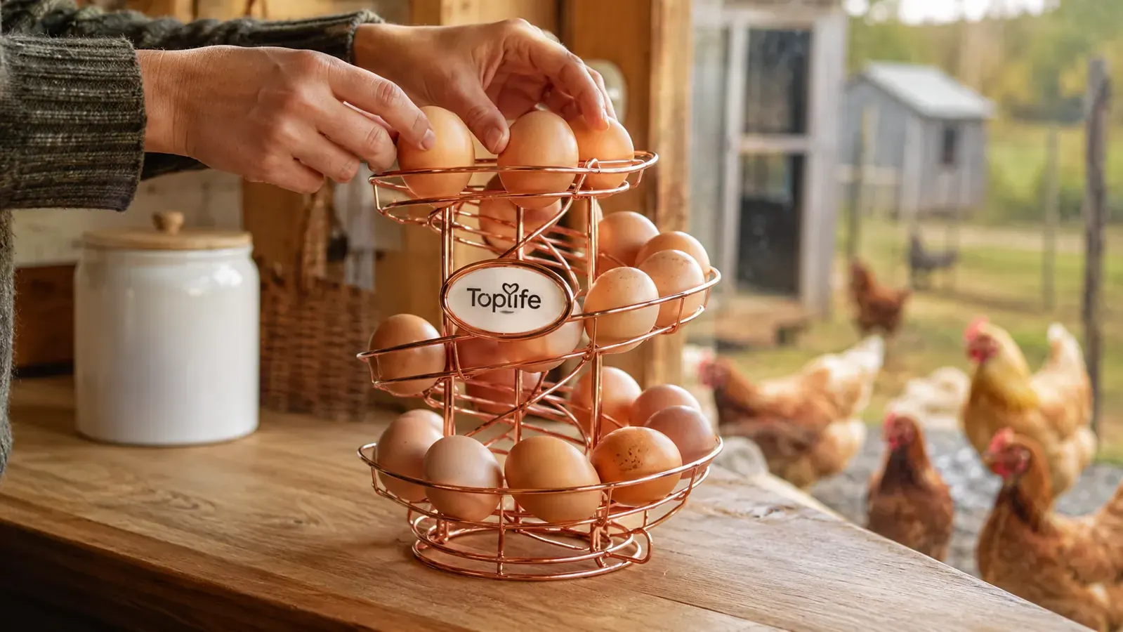 A hand placing two fresh brown eggs onto the top of a rose gold spiral egg skelter rack on the counter